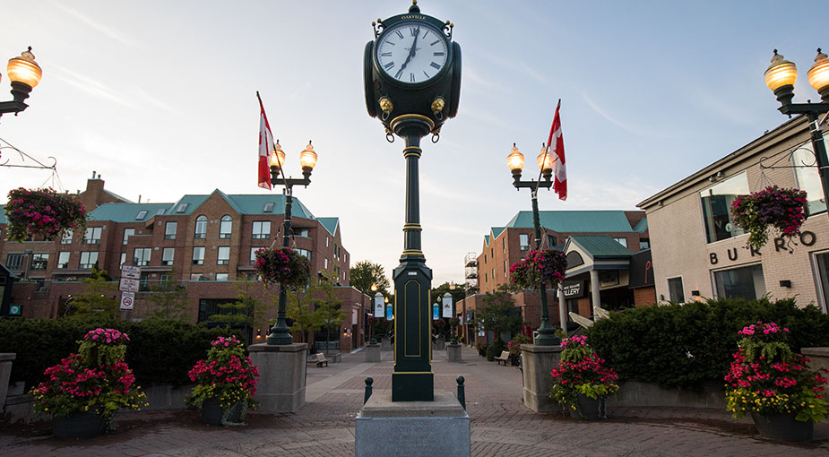 Clock in Towne Square flanked by light posts with Canada flags and hanging flower baskets